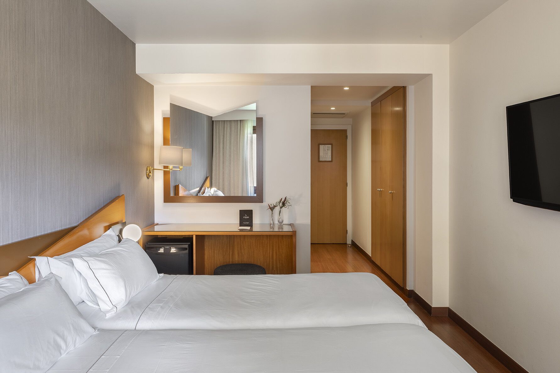 Habitación de hotel con una cama grande, un escritorio con lámpara, un espejo y un televisor montado en la pared.