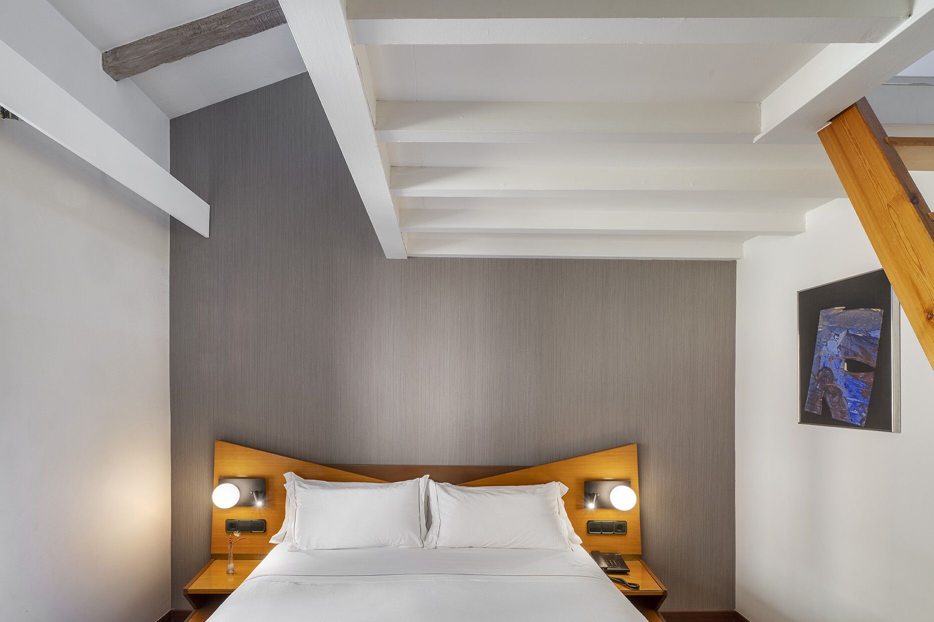 Une chambre d’hôtel moderne avec un grand lit, une tête de lit en bois, deux tables de chevet avec des lampes et un tableau au mur.