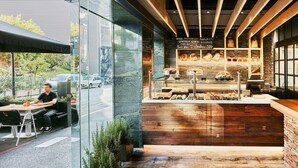 A bakery counter with a variety of baked goods displayed, a seating area with a person, and a view of the street outside. - Hotel de l'Isard (Andorra la Vella)