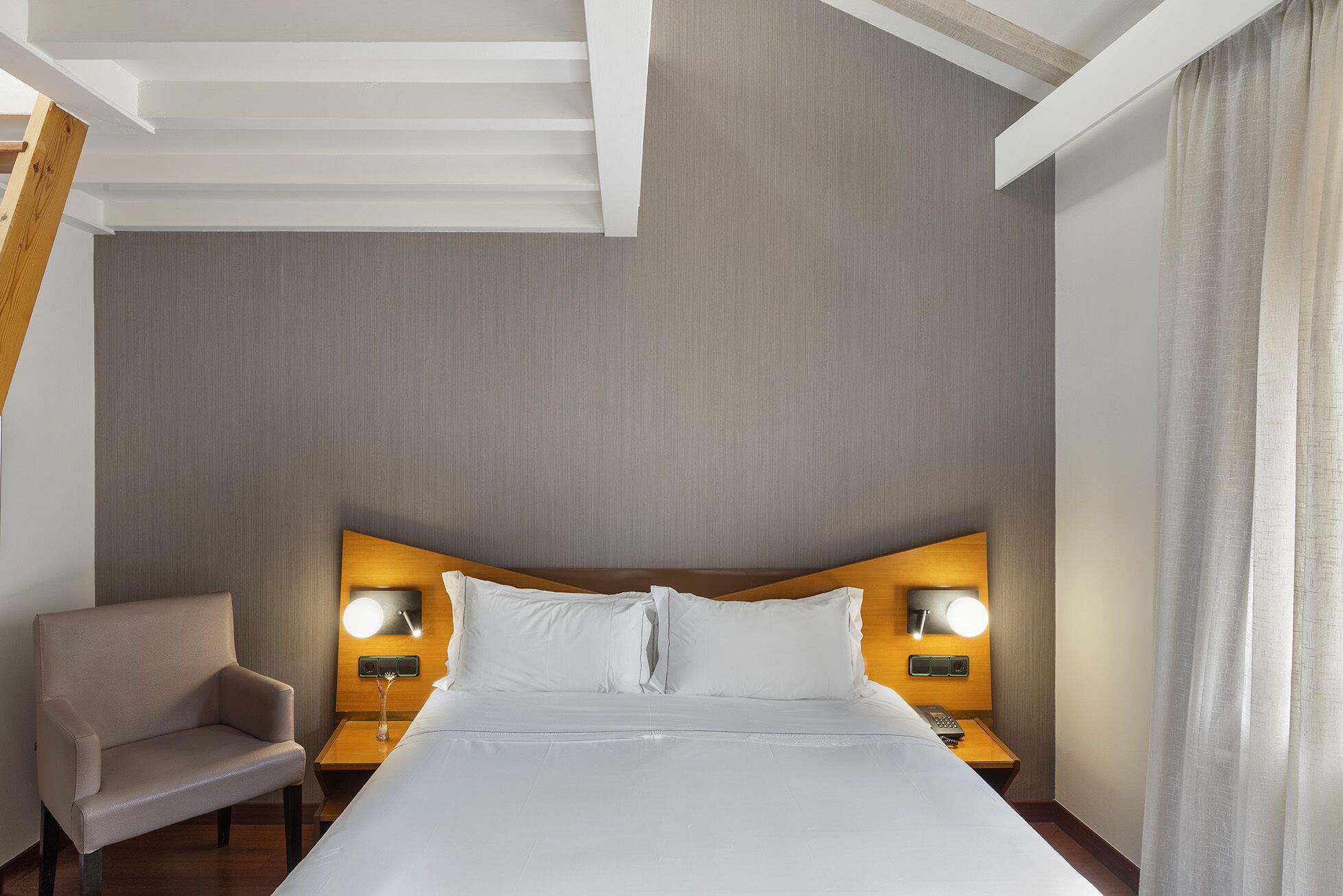 A hotel room with a large bed, two bedside tables with lamps, a chair, and a wooden headboard.