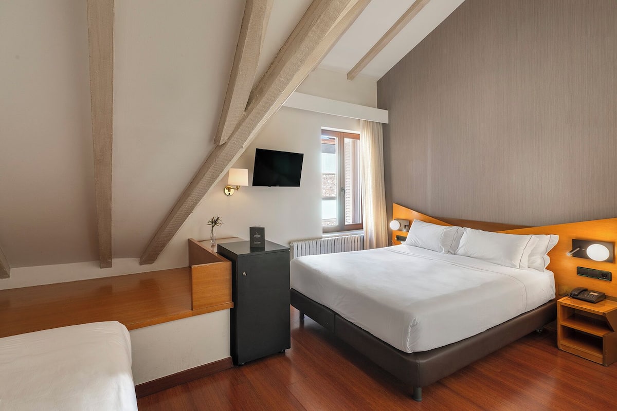 Ein modernes Hotelzimmer mit einem Bett, Nachttisch, Lampe und einem an der Wand montierten Fernseher.