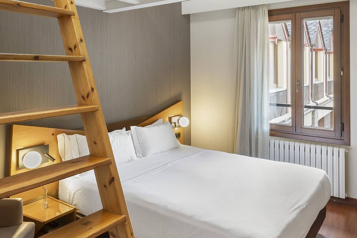Ein Schlafzimmer mit einer Holzleiter, einem Bett, einem Nachttisch und einem Fenster mit Vorhängen.
