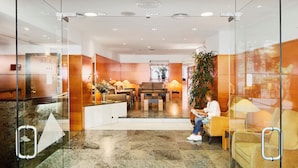 A modern lobby with glass walls, a reception desk, seating area, and a large plant. - Hotel de l'Isard (Andorra la Vella)