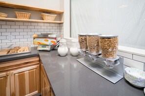 A breakfast bar with cereal dispensers, a coffee machine, and baskets on shelves. - Minna Hotel (San Francisco)