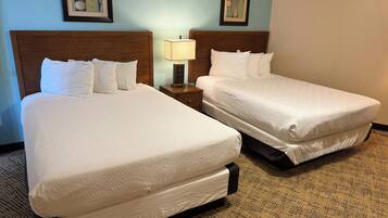 Two double beds with white linens, a nightstand with a lamp, and two framed artworks on the wall.