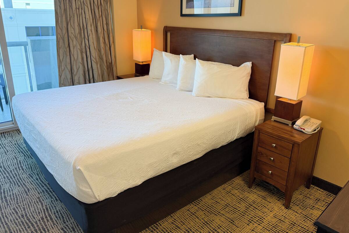 A hotel room with a large bed, two bedside lamps, a wooden nightstand, and a framed picture on the wall.