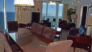 A hotel room with a large glass table, leather chairs, a television, and a view of the ocean.