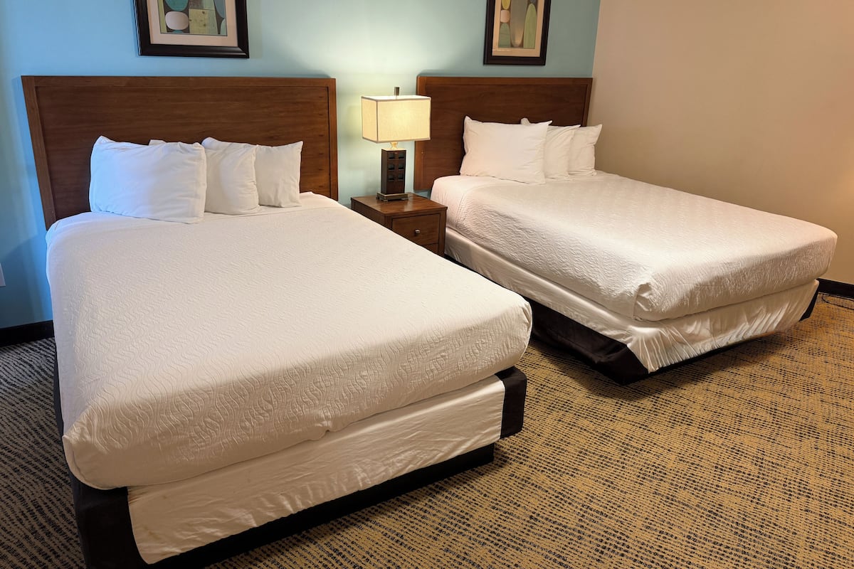 A hotel room with two beds, a nightstand with a lamp, and framed artwork on the walls.