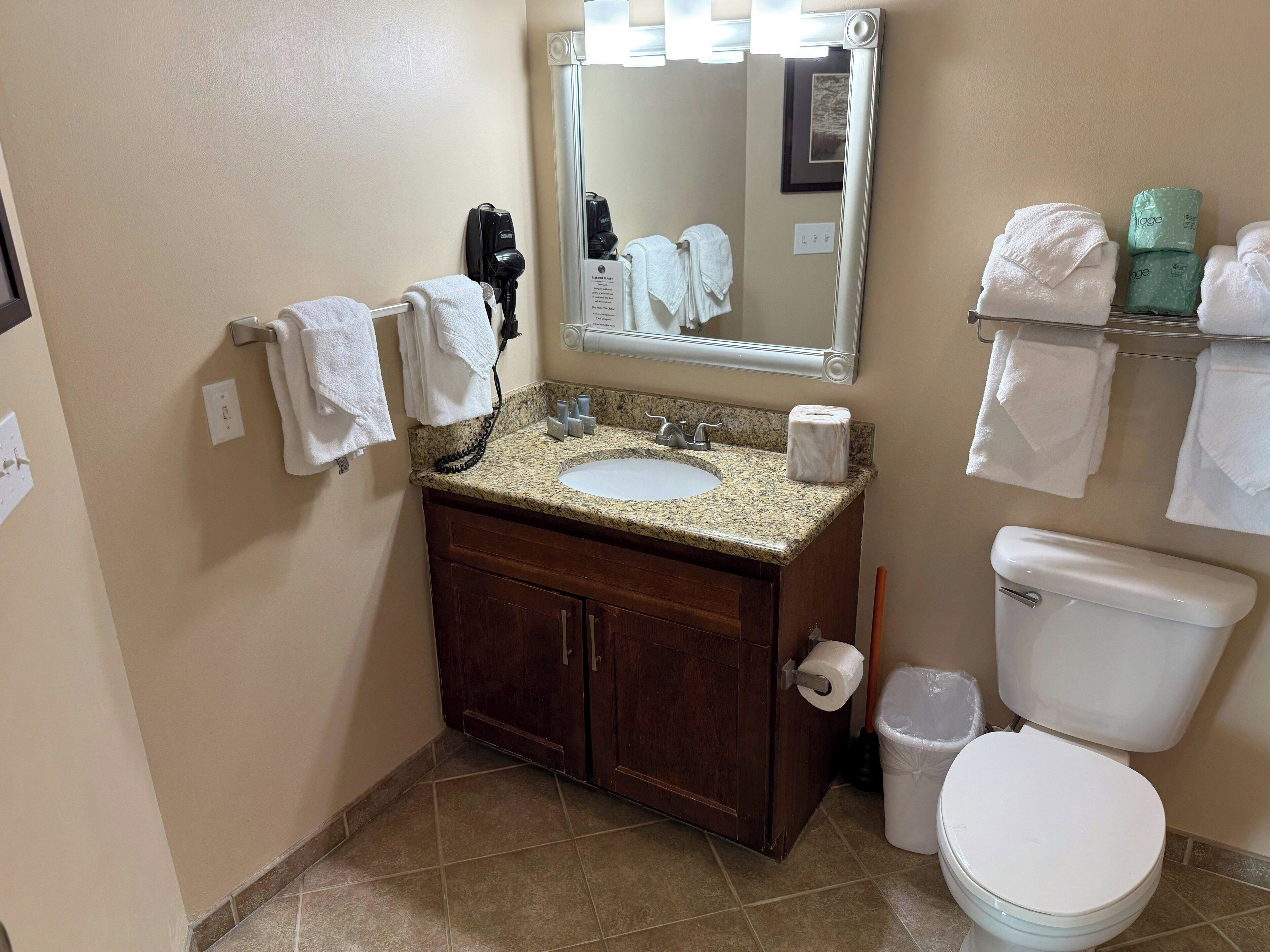 A bathroom with a sink, mirror, towel rack, toilet, and a trash bin.