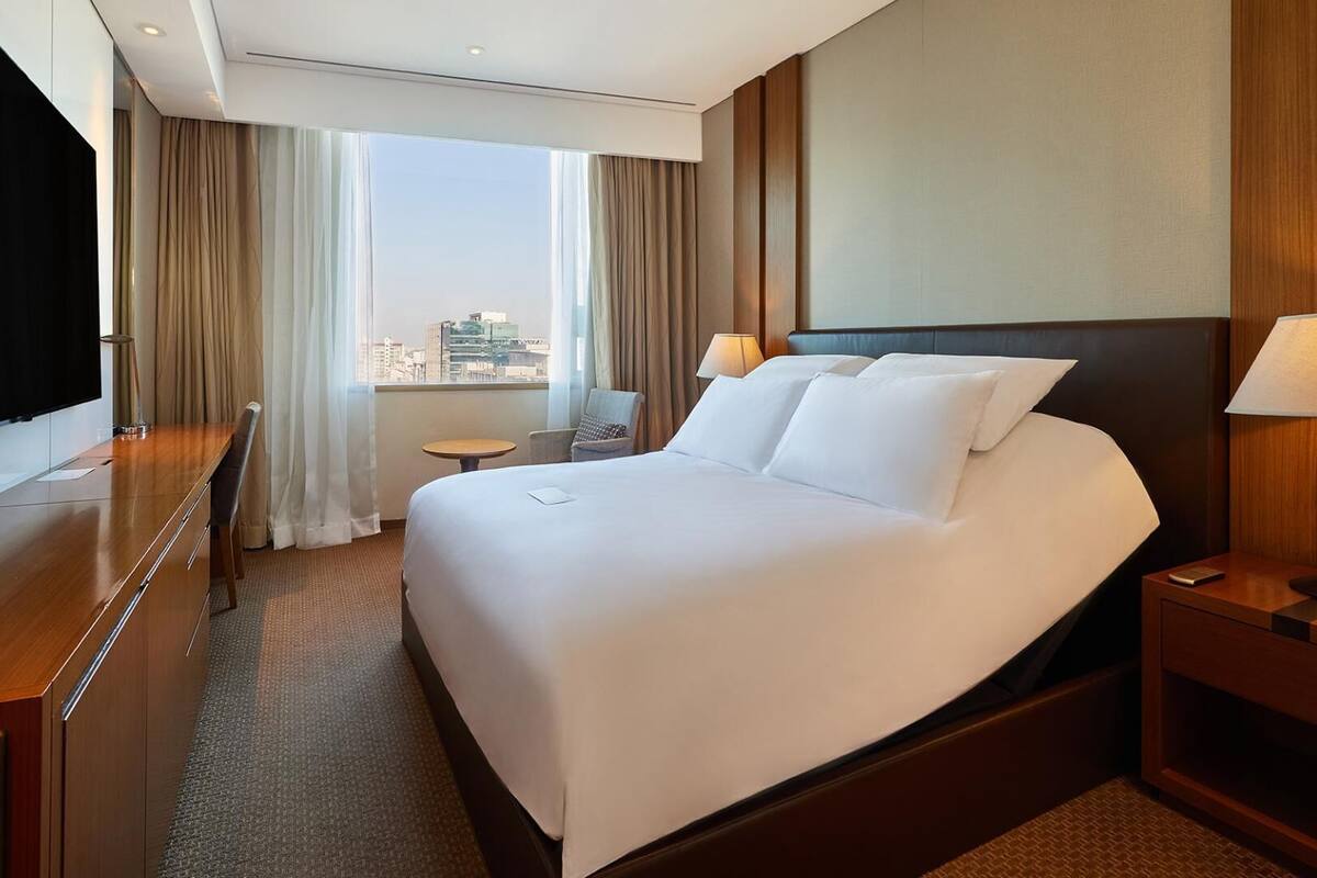 Habitación de hotel con una cama grande, un escritorio, una silla, un televisor y vistas a la ciudad.