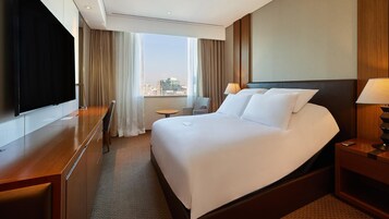 Habitación de hotel con una cama grande, un escritorio, una silla, un televisor y vistas a la ciudad.