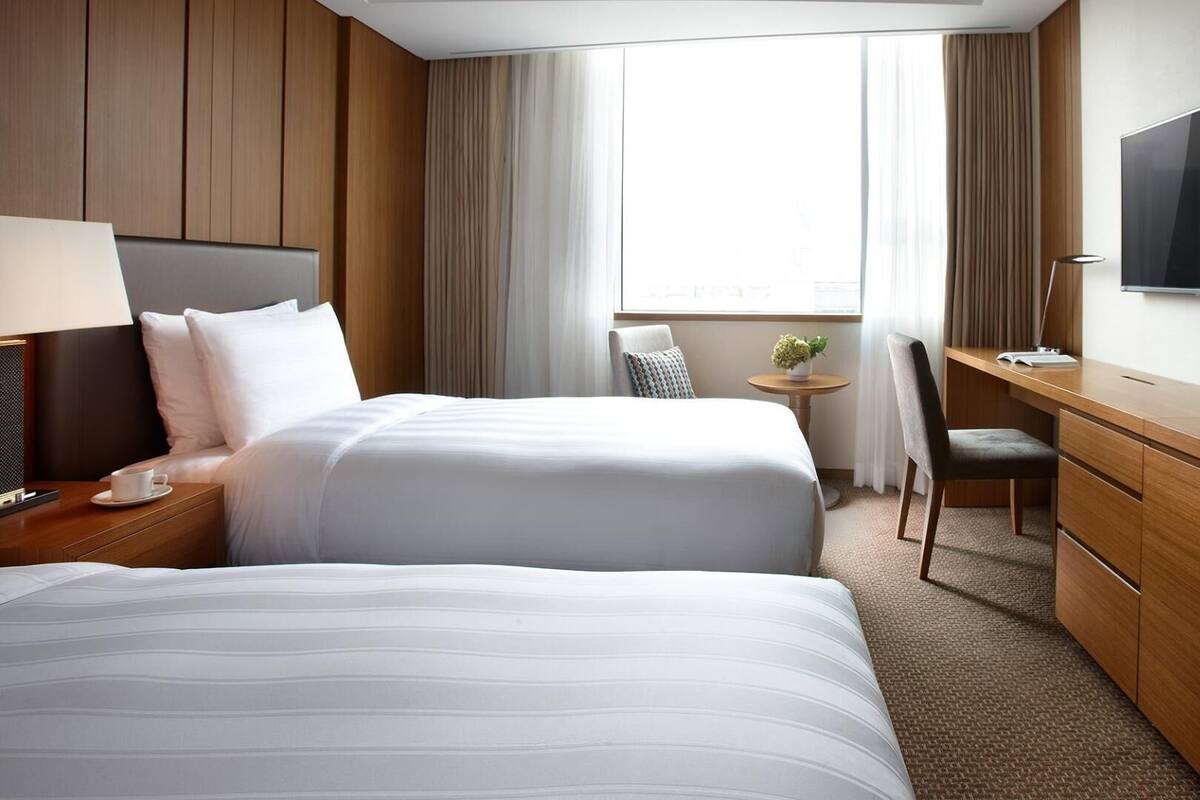 Habitación de hotel con dos camas, un escritorio, una silla, un televisor y una ventana con cortinas.