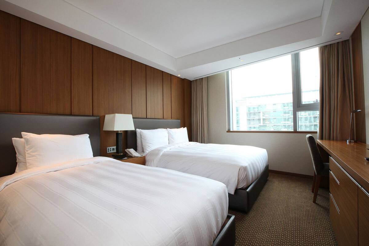 Een hotelkamer met twee bedden, een bureau, een stoel en een groot raam met gordijnen.