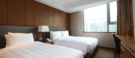 Habitación de hotel con dos camas, un escritorio, una silla y un ventanal con cortinas.