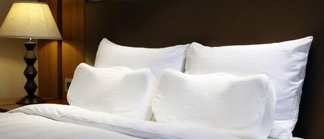 Una cama bien tendida con sábanas y almohadas blancas, un cabecero de madera y una lámpara en una mesita de noche.