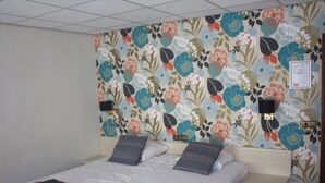 Een hotelkamer met bloemenbehang, een tweepersoonsbed met twee kussens, een nachtkastje met een lamp en een klein nachtkastje met een lamp.