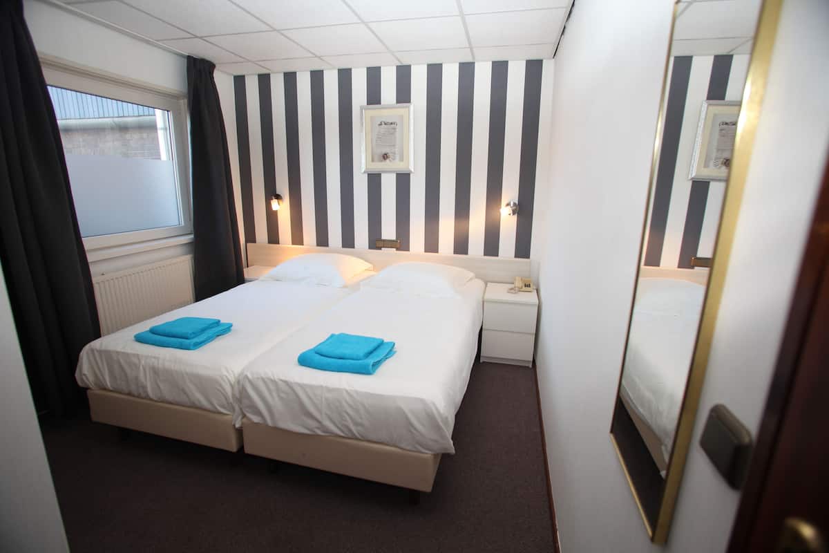 A double bed with two blue towels, a nightstand with a lamp, and a window with curtains.