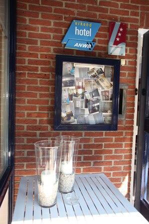 A brick wall with a framed mirror reflecting a room with various items. There is a sign above the mirror that reads "Anwb Hotel" and another sign with a flag. - Het Wapen van Enkhuizen (Enkhuizen)