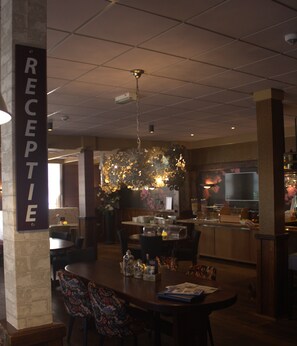 A hotel reception area with a sign reading "RECEPTION," a chandelier, a dining area with tables and chairs, and a kitchen in the background. - Het Wapen van Enkhuizen (Enkhuizen)