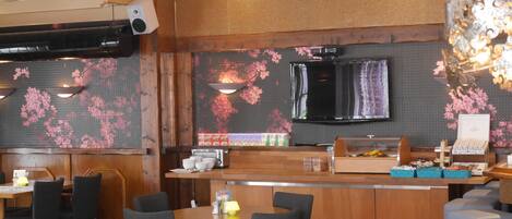 Un restaurante con mobiliario de madera, una barra con vitrina y un televisor montado en la pared.