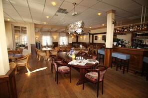 A spacious dining area with wooden tables and chairs, a bar with stools, and a chandelier. - Het Wapen van Enkhuizen (Enkhuizen)