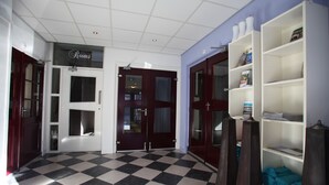 Een hotellobby met zwart-wit geruit tapijt, een receptiebalie en een boekenplank met diverse voorwerpen.