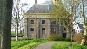Een historisch gebouw met een grindpad dat naar de ingang leidt, omringd door bomen en groen.