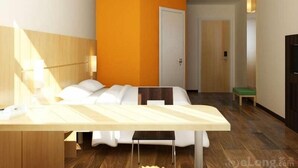 A modern hotel room with a bed, a desk, and a chair. There is a door and a small table with a green cushion. - Ibis Changchun Jianshe Street (Changchun)