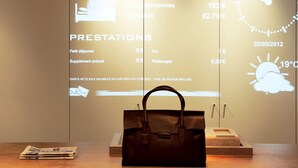 A reception desk with a digital display showing tariffs and services, a clock, and a handbag on the counter. - Ibis Changchun Jianshe Street (Changchun)