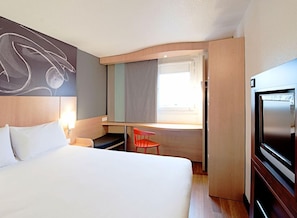 Een hotelkamer met een groot bed, een bureau, een stoel, een televisie en een raam met gordijnen.