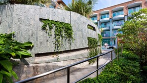 A modern building with a stone facade, a metal railing, and lush greenery. - Ramaburin Resort (Patong)