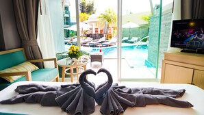 A hotel room with a bed, a TV, a pool view, and a heart-shaped towel arrangement. - Ramaburin Resort (Patong)