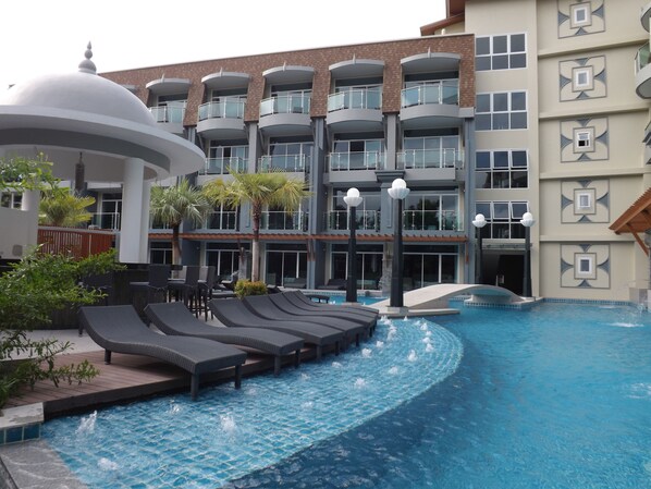 A swimming pool with lounge chairs and a building with multiple balconies. - Ramaburin Resort (Patong)