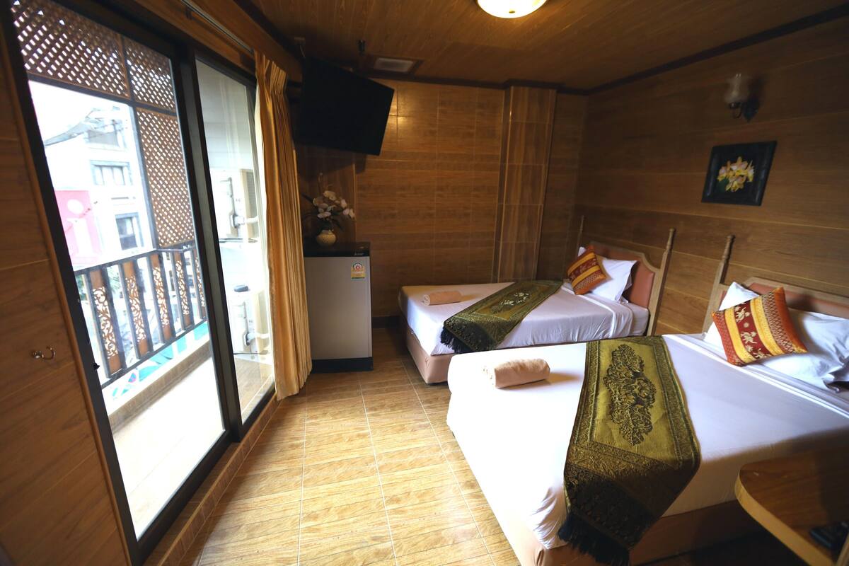A hotel room with two beds, a small table, a TV, and a sliding glass door to the outside.