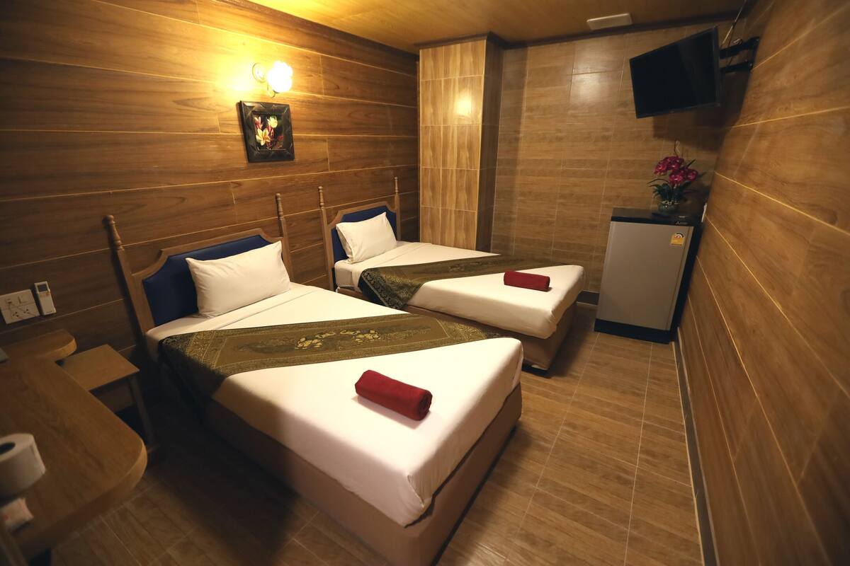 A hotel room with two beds, wooden walls, a small kitchenette, and a television mounted on the wall.