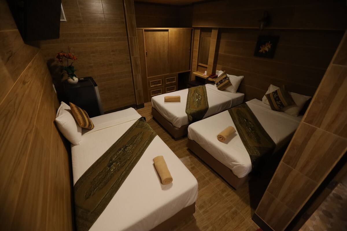A hotel room with two single beds, a wooden wardrobe, a small table with a vase of flowers, and a mirror on the wall.