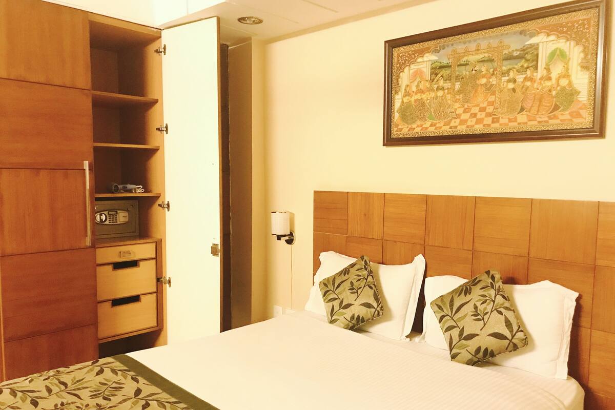 Una habitación de hotel con una cama, un armario, un cuadro en la pared y una mesita de noche con una lámpara.