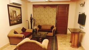Una sala de estar con dos sofás, una mesa de centro, un tapete estampado, un televisor sobre un mueble bajo y una puerta.