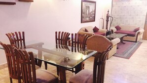 Un área de comedor con una mesa de vidrio rodeada de sillas de madera, un sofá con cojines y un cuadro en la pared.