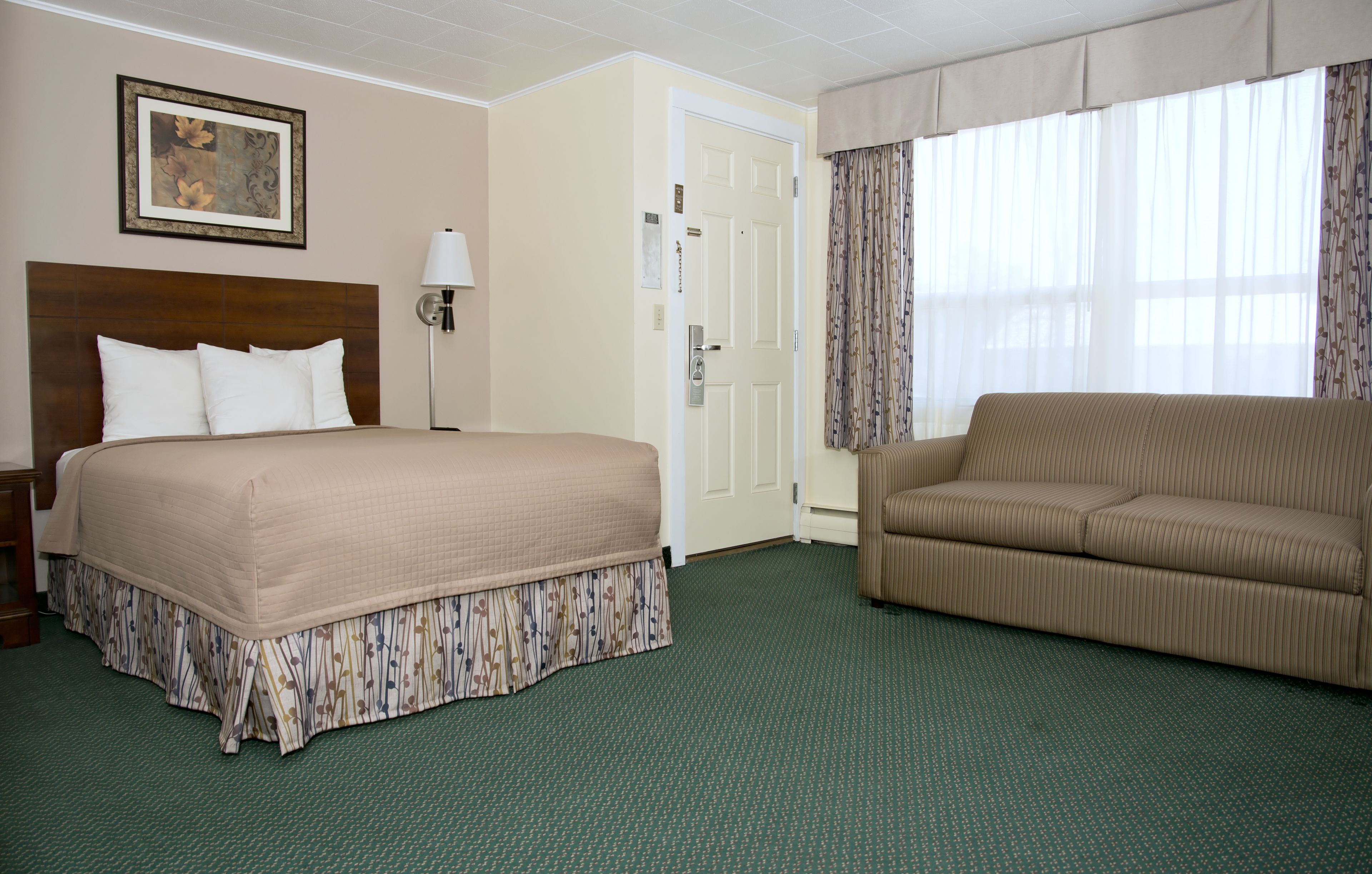 A hotel room with a large bed, a sofa, a framed picture on the wall, and a door.