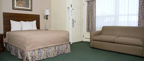 A hotel room with a large bed, a sofa, a framed picture on the wall, and a door.