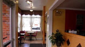 A hotel lobby with a reception desk, a dining area with a table and chairs, a potted plant, and a view of the street through large windows. - Travelers Inn (Brunswick)