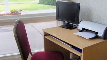Un escritorio con monitor de computadora, impresora y silla frente a una ventana.