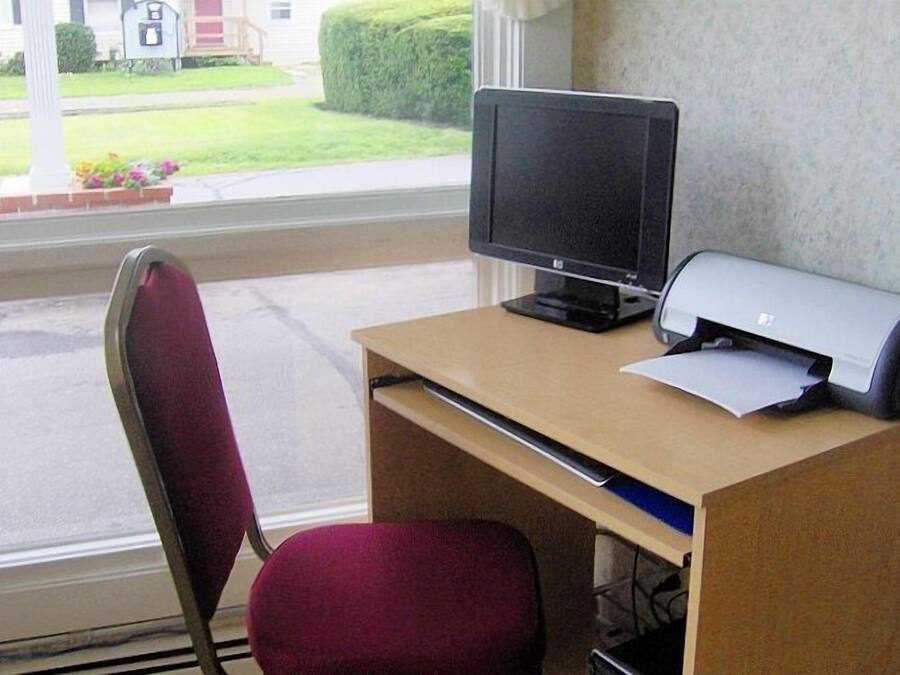 A desk with a computer monitor, printer, and chair in front of a window.