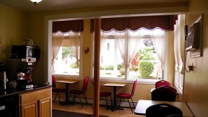 A cozy kitchen with a coffee machine, a dining area with chairs, and large windows with curtains. - Travelers Inn (Brunswick)