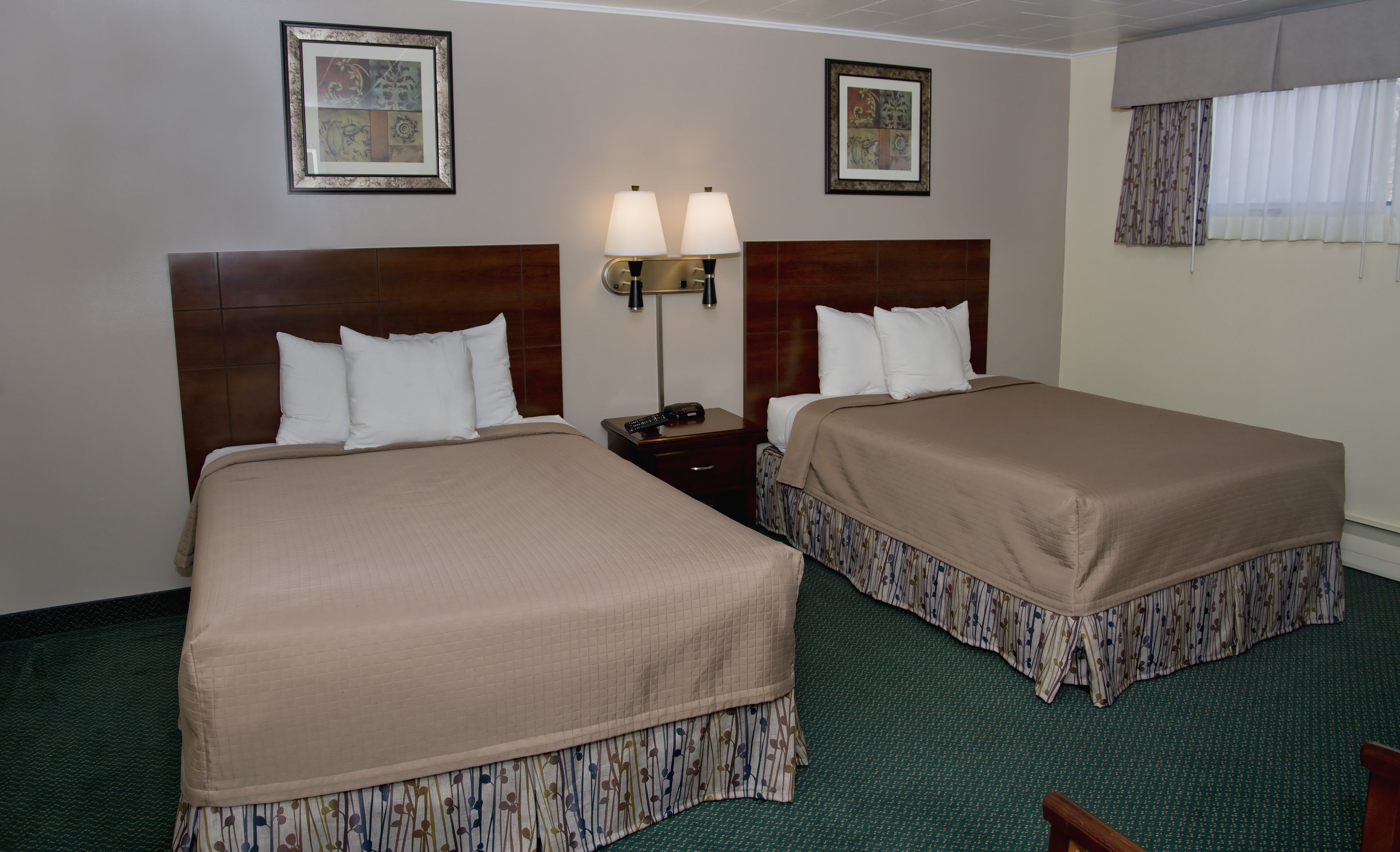 A hotel room with two beds, a nightstand, a lamp, and two framed pictures on the wall.