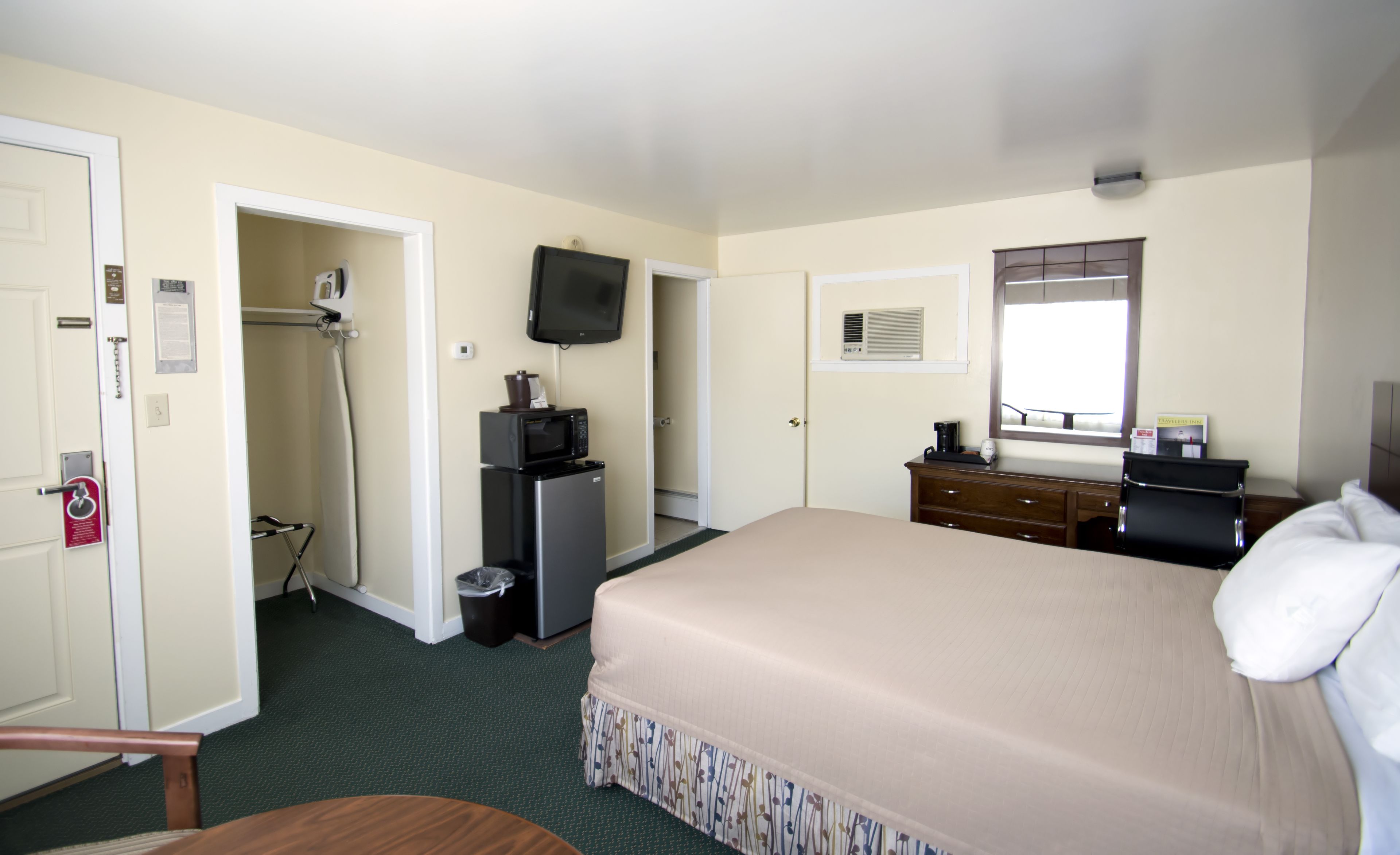 Una habitación de hotel con una cama, un escritorio, un televisor, un espejo y una puerta que da a un baño.