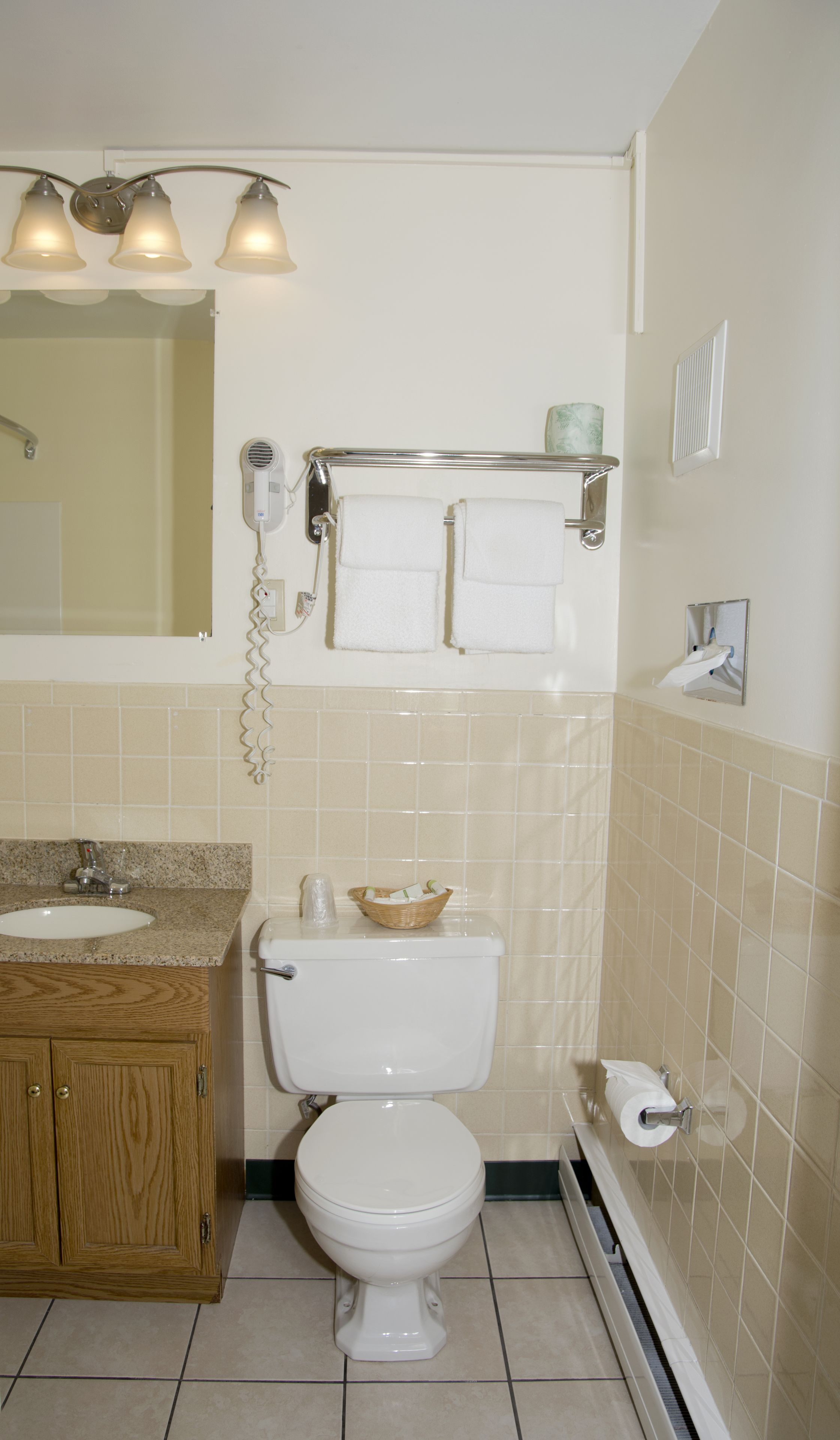 Un baño con inodoro, lavamanos, tocador, toallero y espejo.