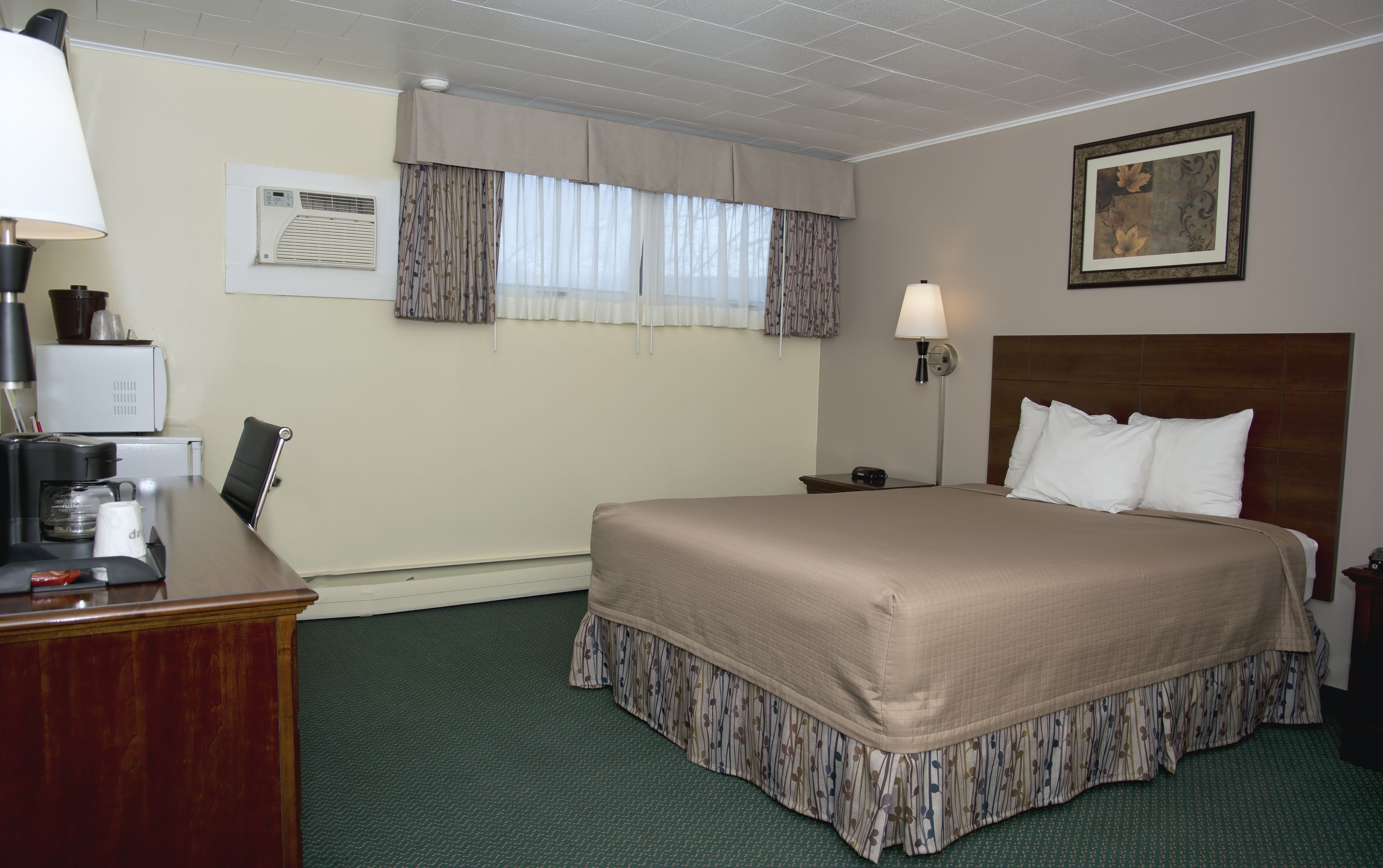 Een hotelkamer met een bed, een bureau met koffiezetapparaat, een lamp en een schilderij aan de muur.