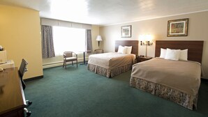 A hotel room with two beds, a desk, a chair, and a window with curtains.